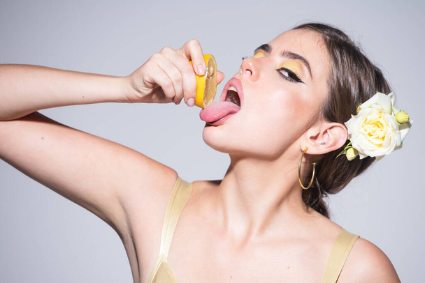 Pretty girl or sexy woman with stylish makeup on beautiful face squeezing juice from fresh orange citrus fruit, lick with tongue natural orange juice - Photo, Image