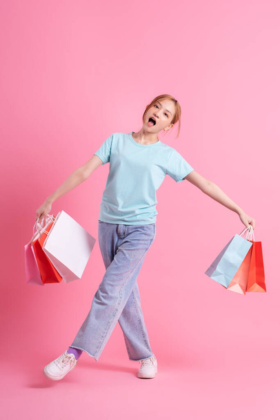 jong aziatische vrouw holding shopping tas op roze achtergrond - Foto, afbeelding