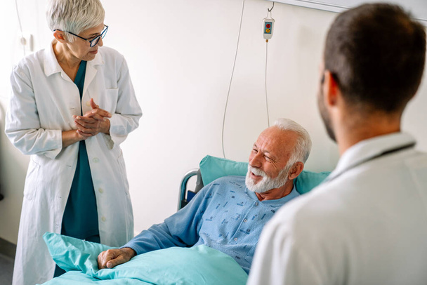 Doctor talking to senior male patient in hospital bed who is recovering from the disease. Healthcare, coronavirus, people concept. - Foto, afbeelding