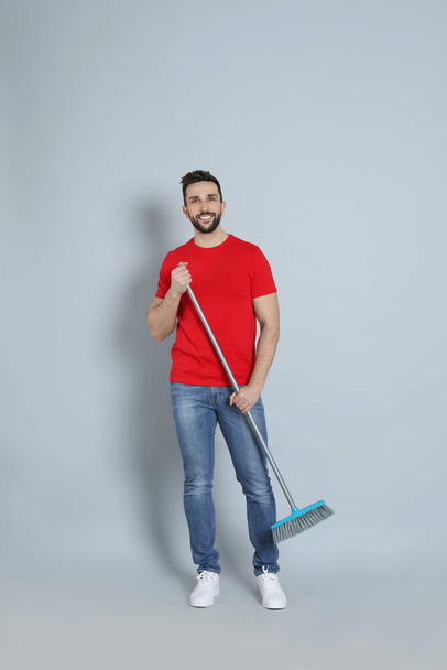 Handsome man with broom on grey background - Fotó, kép