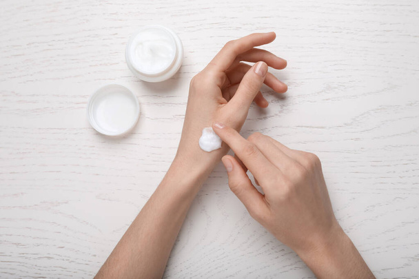 Woman applying body cream onto her wrist at white wooden table, top view - Foto, Imagem