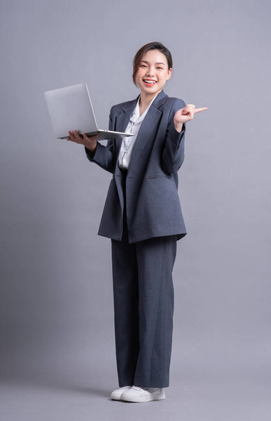 Giovane donna d'affari asiatica in piedi su sfondo grigio - Foto, immagini