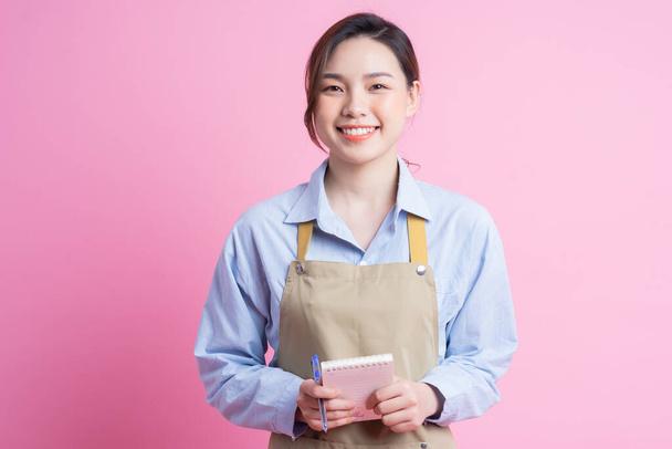 Young Asian waitress standing on pink background - Фото, изображение
