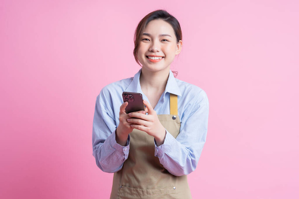 Joven camarera asiática de pie sobre fondo rosa - Foto, Imagen