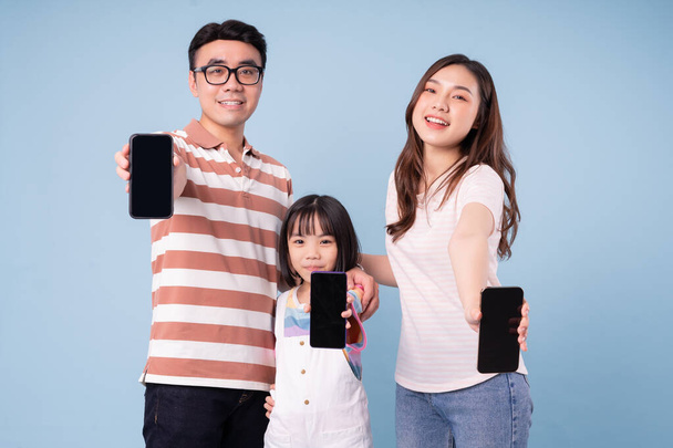 Mavi arka planda akıllı telefon kullanan genç Asyalı aile görüntüsü - Fotoğraf, Görsel