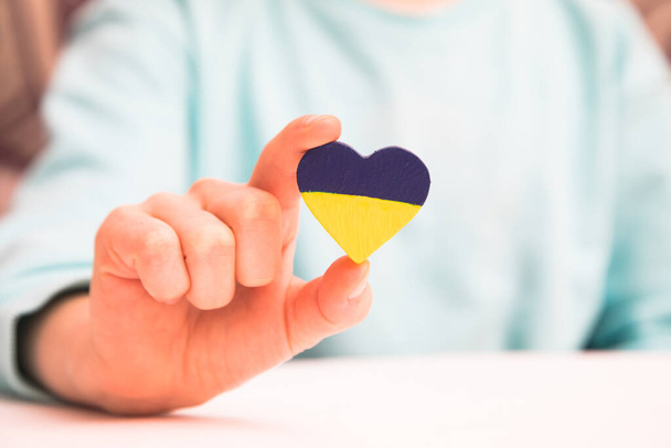 High angle view of child hands holding ukraine flag painted heart - Φωτογραφία, εικόνα