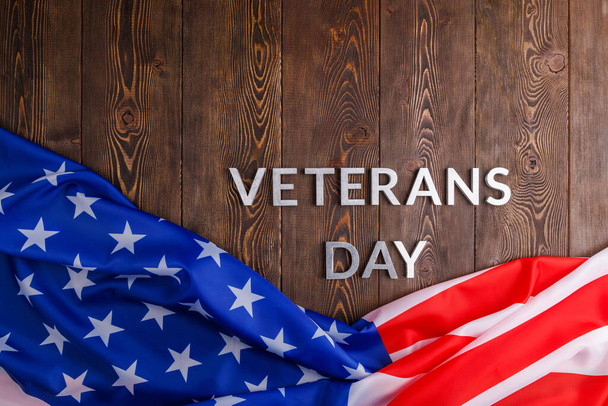 the words veterans day laid with silver metal letters on wooden board surface with crumpled usa flag - Zdjęcie, obraz
