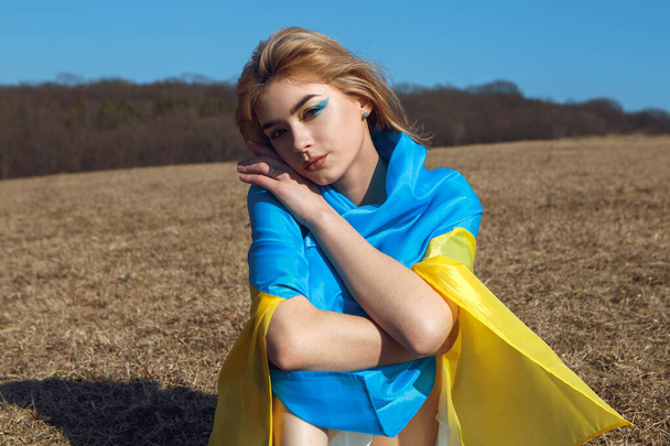 Ukrayna sarısı mavi bayrağa sarılı kadın portresi rüzgarda dalgalanıyor. Ukrayna 'nın ulusal sembolü. Makyajlı vatansever kadın. Ukrayna, destek ve dayanışma - Fotoğraf, Görsel