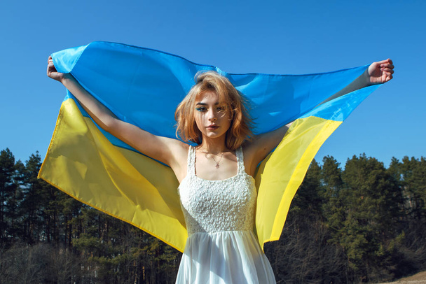 Портрет жінки, загорнутої в україно-жовті прапори, коливається на вітрі. Національний символ України. Патріотична пані з косметикою. Стань з Україною, підтримка і солідарність. - Фото, зображення