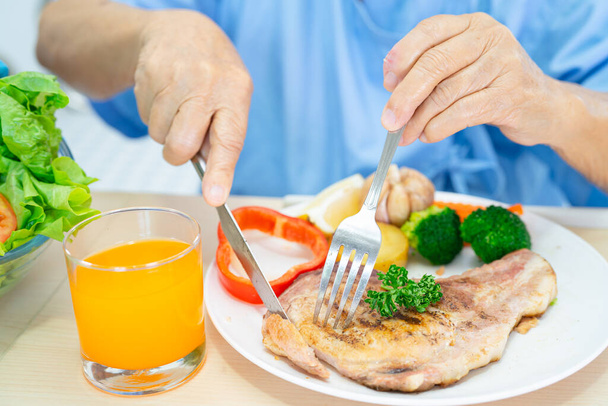 Asiatique personne âgée ou âgée femme âgée patient manger le petit déjeuner et légumes alimentation saine avec espoir et heureux tout en étant assis et affamé sur le lit à l'hôpital. - Photo, image