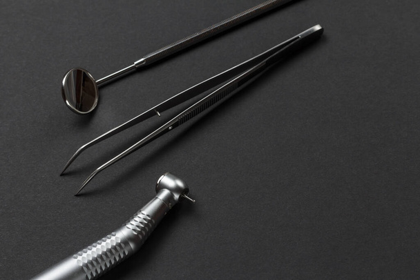Head of high-speed dental handpiece with bur, a metal mirror and a tweezers on the black background. Dental instruments for dental treatment. Top view. - Photo, Image