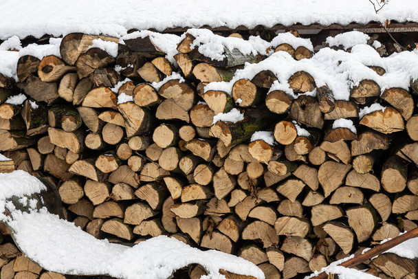 Snow covered firewood. Stack of wood cut. Snow on the timber stack. Wooden log store under snow. - Photo, Image