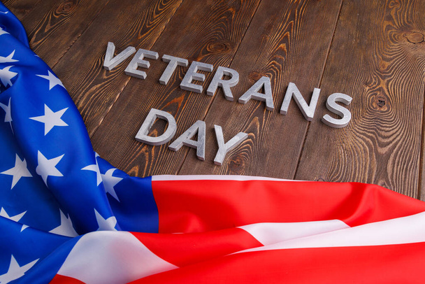 the words veterans day laid with silver metal letters on wooden board surface with crumpled usa flag - Fotografie, Obrázek