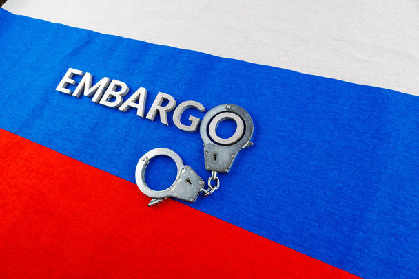 the word embargo laid with silver metal letters on russian tricolor flag with silver handcuffs - Foto, Imagen