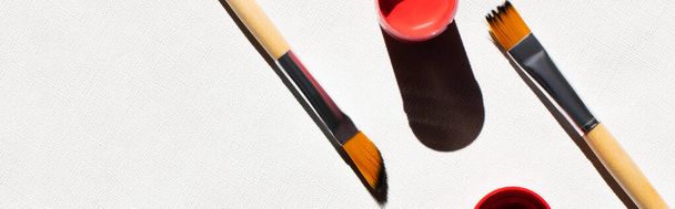 top view of paintbrushes near red paint on white textured background, banner - 写真・画像