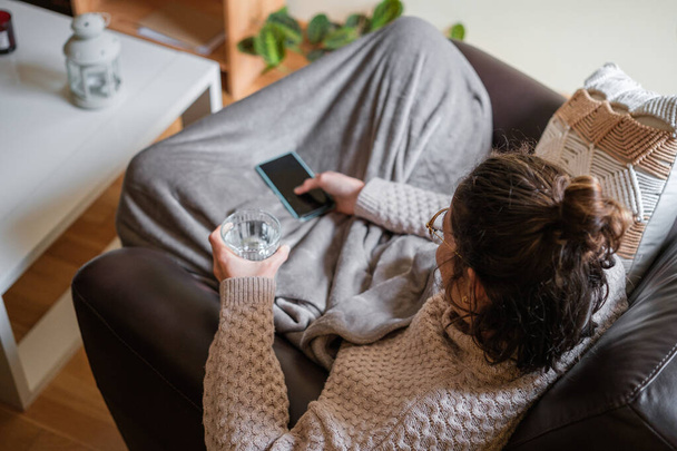 Top view of woman with sore throat resting on the couch with a glass of water. - Photo, Image