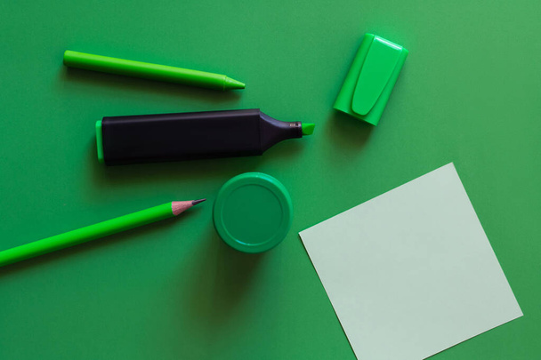 vista superior de lápiz, crayón, tarro con pintura y rotulador cerca de la nota de papel en verde - Foto, imagen