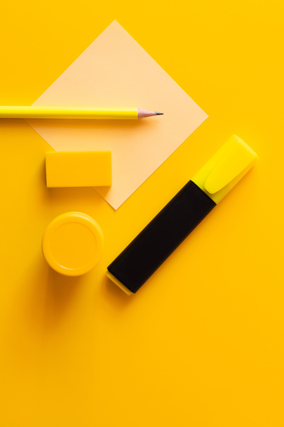 πάνω όψη της γόμα, μολύβι, βάζο με χρώμα και μαρκαδόρο στυλό κοντά σε χαρτί σημείωμα σε κίτρινο - Φωτογραφία, εικόνα