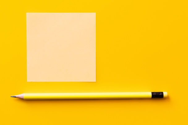 top view of sharp pencil near blank paper note on yellow - Фото, изображение