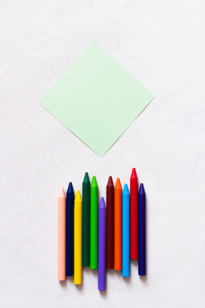 vue de dessus des crayons colorés près de la note de papier vide sur fond blanc texturé  - Photo, image