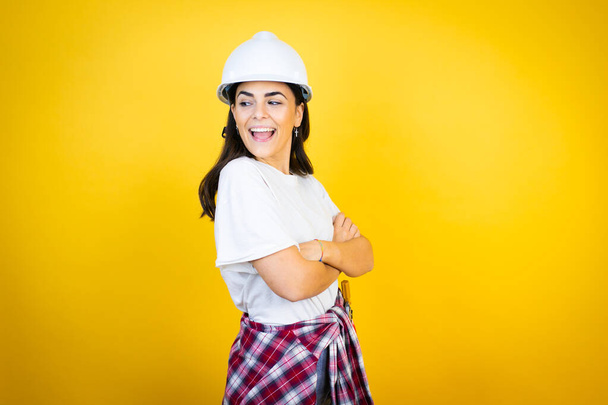 Jeune femme caucasienne portant un casque et des vêtements de constructeur sur fond jaune isolé regardant vers le côté, pose de profil relax avec le visage naturel et sourire confiant. - Photo, image