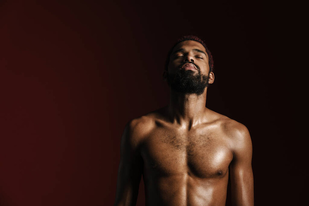 Black shirtless sportsman posing on camera with eyes closed isolated red white background - Φωτογραφία, εικόνα
