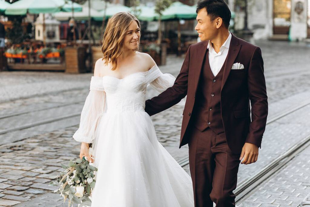 An international wedding couple, a European bride and an Asian groom walk around the city together. - Foto, Imagem