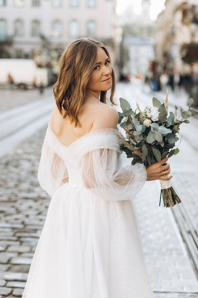 Beautiful bride with a bouquet posing in the city streets - Foto, Imagen