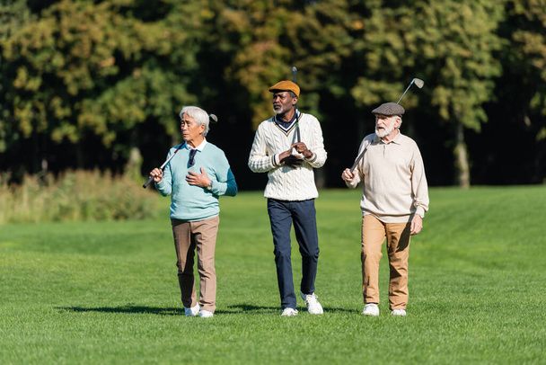 Senioren laufen mit Golfschlägern auf der grünen Wiese - Foto, Bild