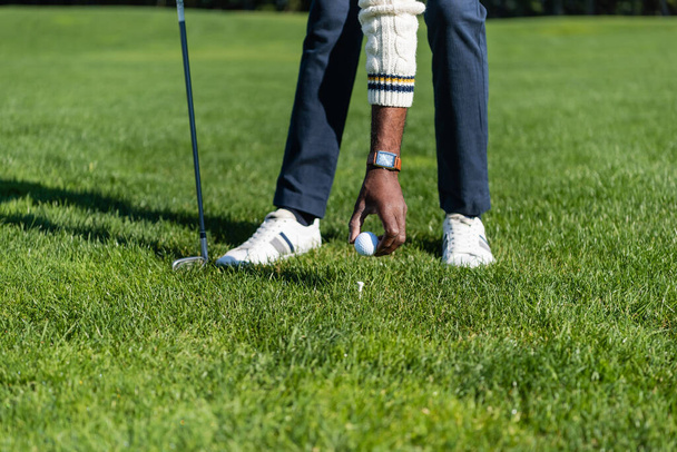 vista recortada del hombre afroamericano colocando pelota en la camiseta de golf - Foto, Imagen