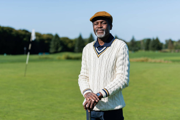fröhlicher afrikanisch-amerikanischer Mann steht mit Golfschläger auf der grünen Wiese - Foto, Bild