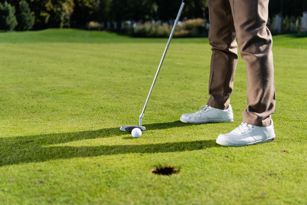 Kırpılmış beyaz spor ayakkabılı bir adamın çimlerde golf oynaması. - Fotoğraf, Görsel