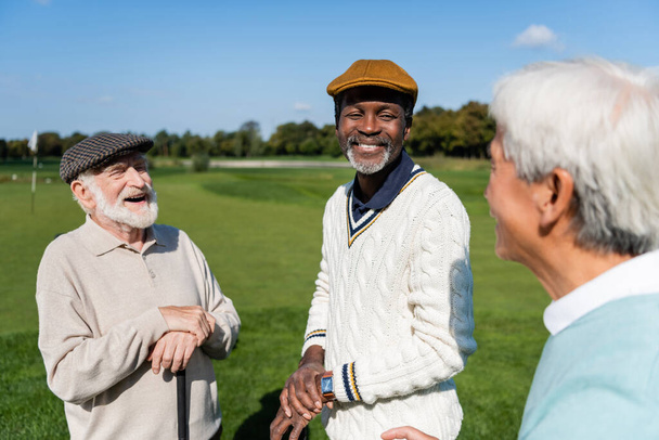 happy and senior multiethnic men looking at blurred asian friend  - 写真・画像