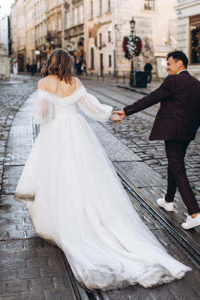 An international wedding couple, a European bride and an Asian groom walk around the city together. - Zdjęcie, obraz