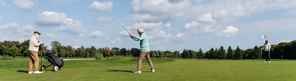 senior asian man playing golf near friends with flag stick and golf cart, banner - Фото, изображение