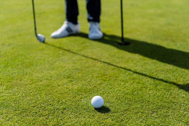 Golfball auf grünem Rasen neben verschwommenem Mann  - Foto, Bild