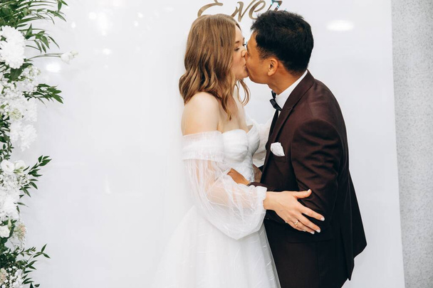 Stylish pretty bride and asian groom kissing on the wedding  - Foto, Imagen