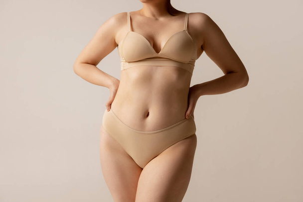 Cropped portrait of natural looking female body in beige underwear posing isolated over light studio background - Foto, Bild