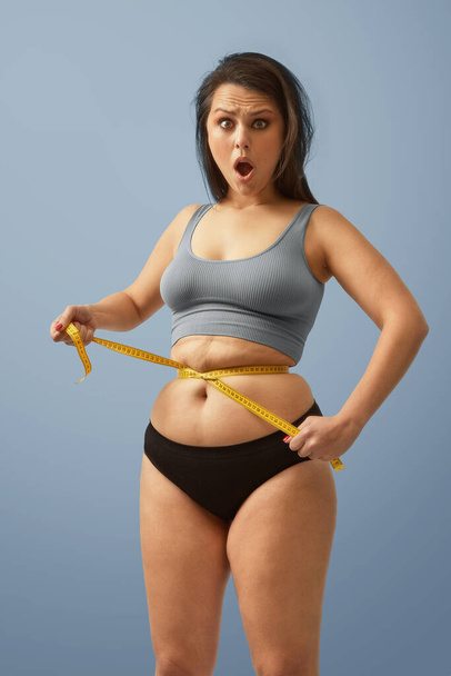Здивована надмірна вага кавказької жінки обмотує мірну стрічку навколо талії. Високоякісне зображення фотографій
. - Фото, зображення