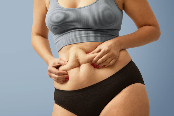 Upset plus size female on squeezing her abdomen excess fat. High quality studio photo image jpg - Photo, Image