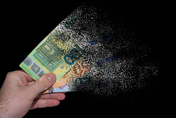 три банкноты евро, удерживаемые в одной руке, разлагаются и растворяются из-за инфляции на черном фоне - Фото, изображение