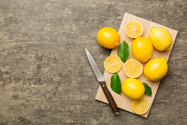 Top view with copy space for fresh and ripe lemons on cutting board. Healthy food background. Elegant background of lemon and lemon slices with squeezer and knife colored background. - Photo, Image