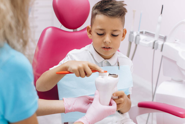Female dentist shows a boy on a mock-up how to brush his teeth properly - Photo, Image
