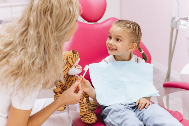 Kislány egy látogatáson a fogorvosnál, kezében egy játékkal, és bemutatja, hogyan kell fogat mosni egy fogászati klinikán. - Fotó, kép