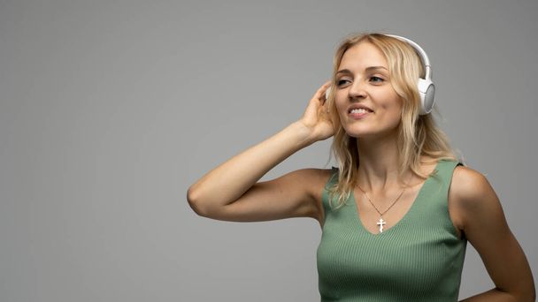 Beautiful blonde girl in green t-shirt in headphones having fun in studio dancing and laughing. - Foto, Imagen
