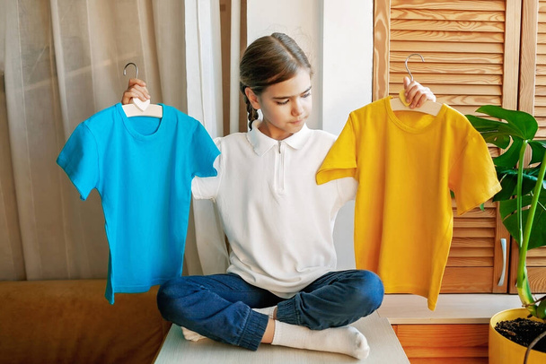 Girl chooses T-shirt among clothes at home. Mockup friendly. T-shirts ready to have design - Фото, зображення