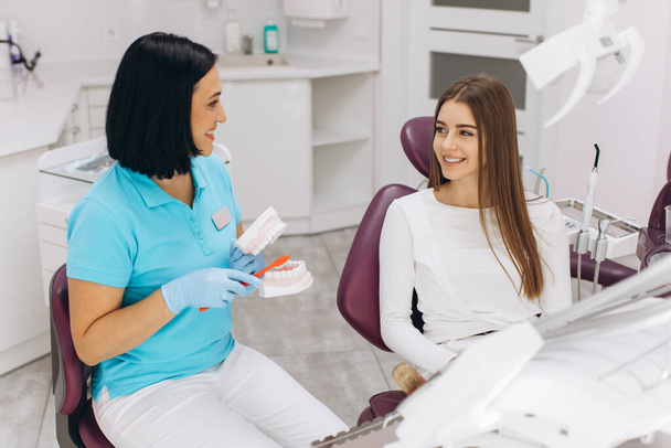 Naispuolinen hammaslääkäri näyttää potilaalle, miten harjata hampaat kunnolla. - Valokuva, kuva