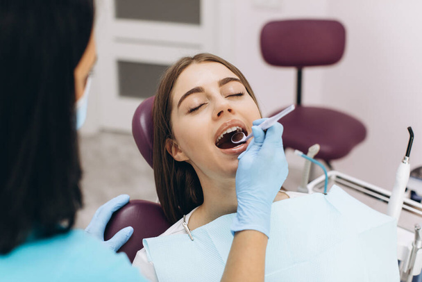 女性歯科医は彼女の患者を歯科椅子で調べる. - 写真・画像