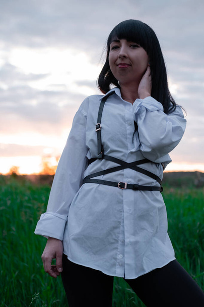 young woman in baldric on the summer field on sunset or sunrise. peaceful calm female. trendy clothes. - Photo, Image