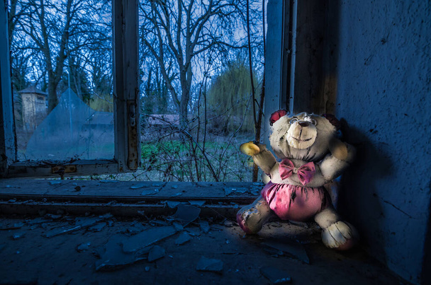 lichtgevende pluche beer staande op de vensterbank van een verlaten huis - Foto, afbeelding